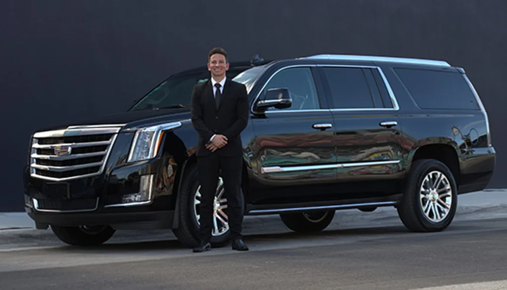 How Luxury Car Services Redefine Your Journey From Mundane to Magnificent? 3 Man in a suit stands beside a black Cadillac SUV, representing a premier luxury car service in Los Angeles